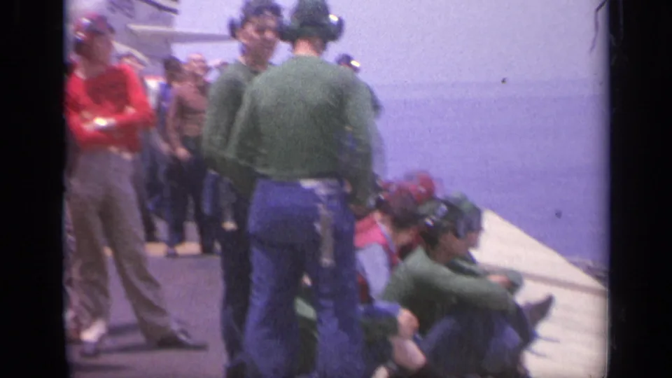 Carrier-deck personnel and visitors appear gathered near the deck edge, with open sea visible in this 1962 Italy home-movie frame.