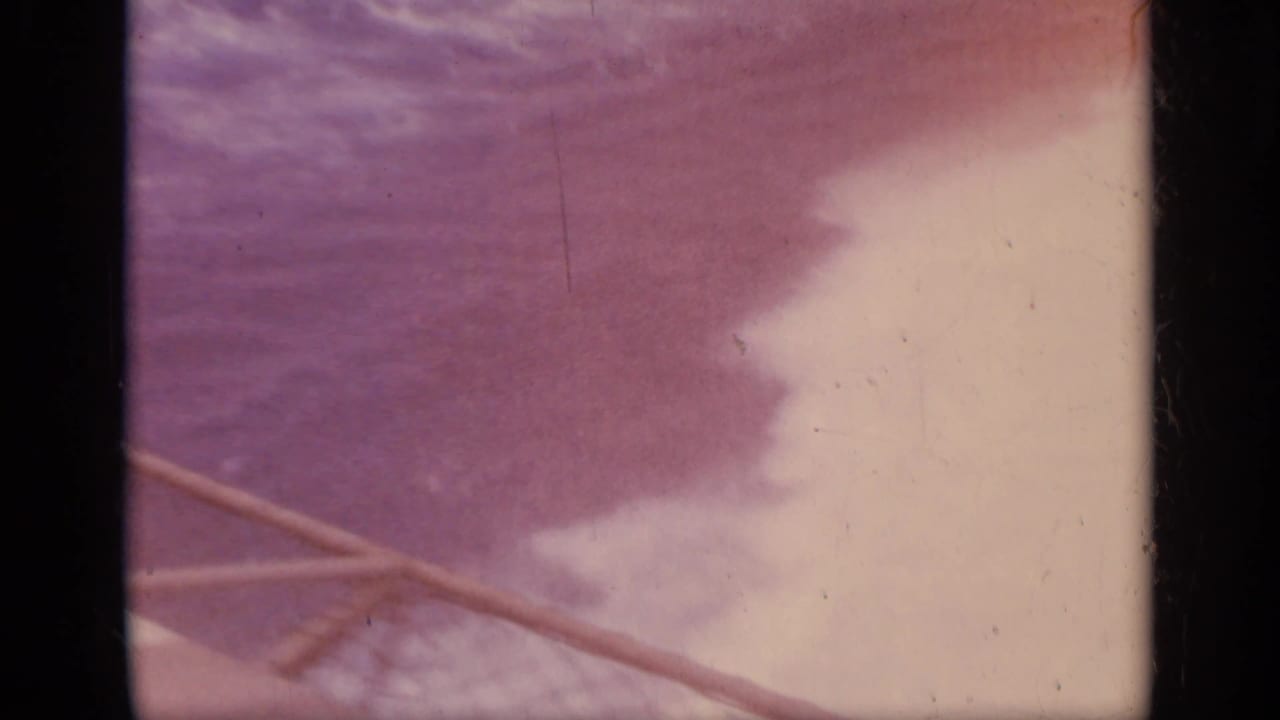 Faded sea and sky seen past a ship railing or line on 8mm film.