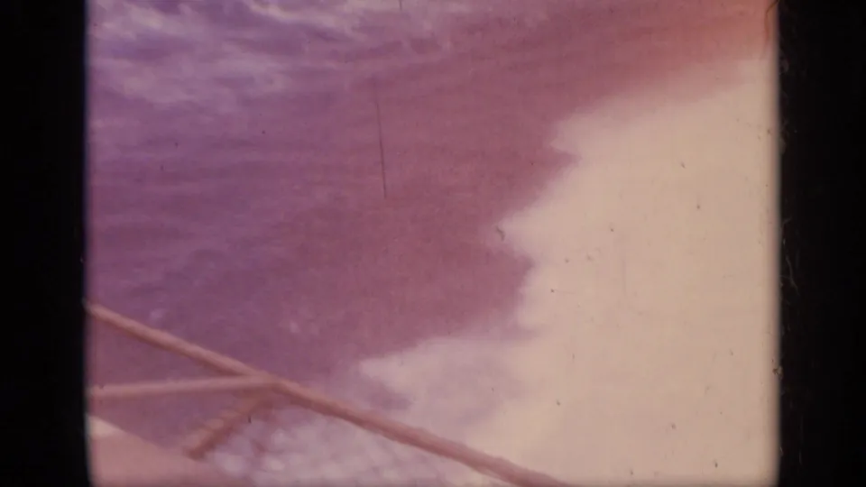 1962 Italy travel footage shows open water and hazy sky past a diagonal ship line or railing, with strong magenta color fading.
