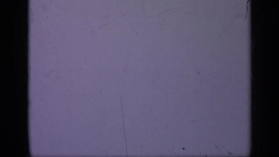1962 Italy 8mm frame showing blue-purple film texture, a dark vertical edge, faint scratches, dust, and gentle light falloff.