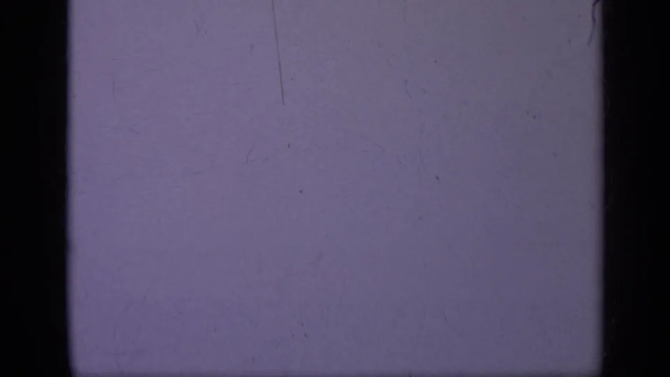 1962 Italy 8mm frame with a purple-blue field, black film borders, faint vertical scratching, dust, and soft grain.