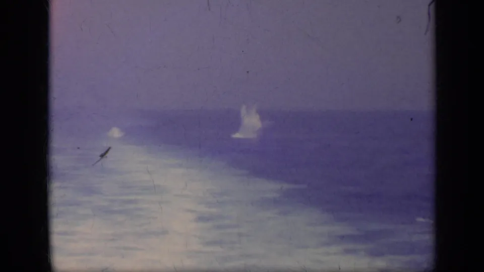 Wide 1962 Italy sea view with a small bright explosion or splash rising from the water, framed by dark 8mm borders and purple color shift.