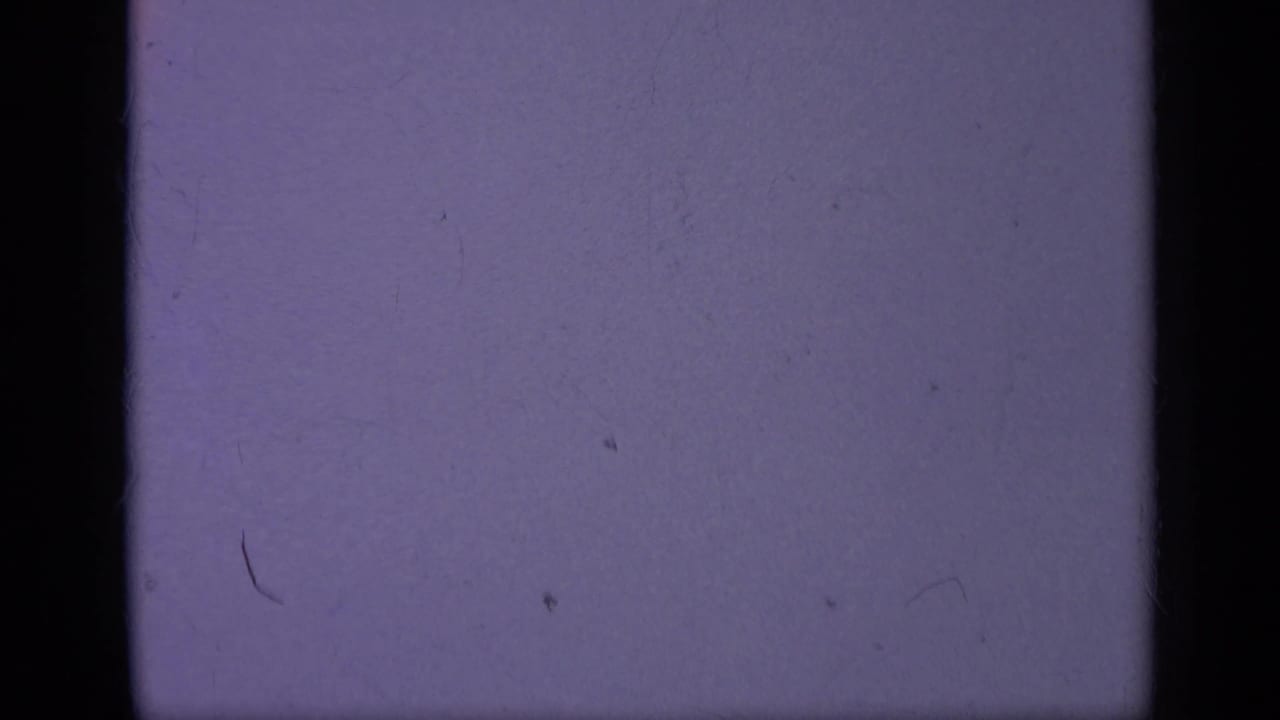 A tiny aircraft sits against the pale purple sky, with 8mm grain, dust, and edge shadowing from the film scan.