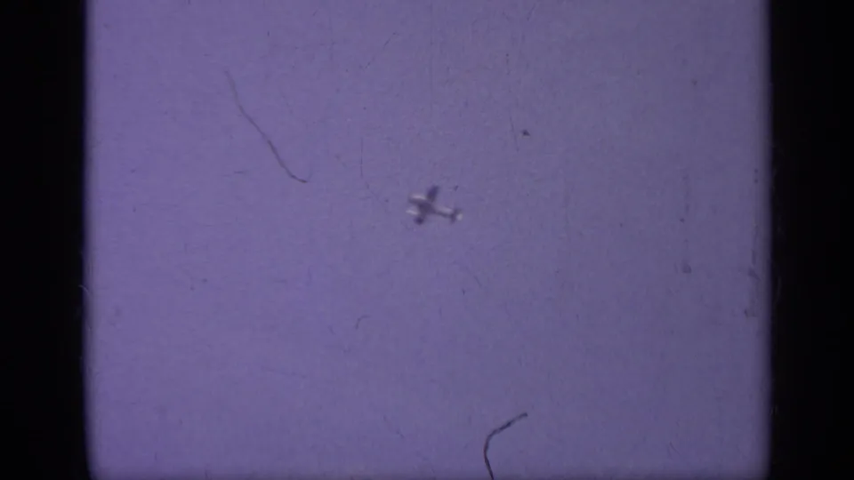 A small airplane is visible against a purple sky in the final frame, with scratches, dust, and dark 8mm gate edges present.