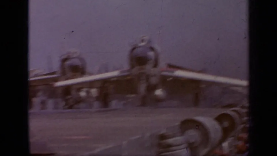 Soft 1962 8mm view from an aircraft carrier deck, with blurred aircraft parts in the foreground and deck hardware beyond.
