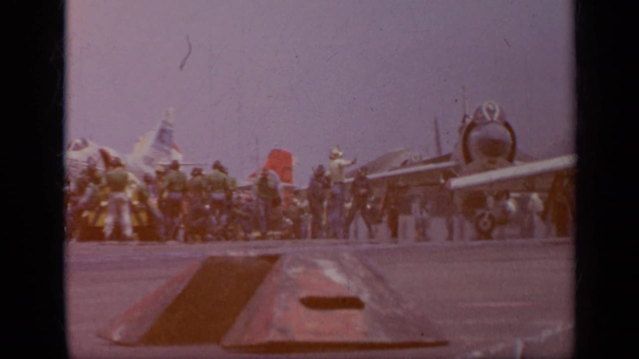 Aircraft lined on a carrier deck with sailors gathered nearby.