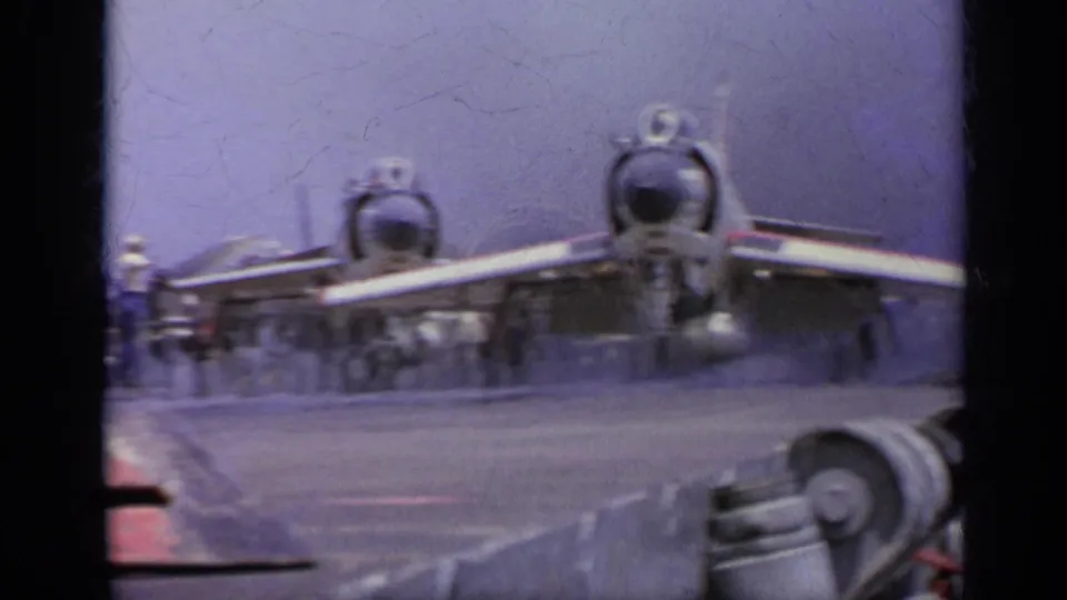 Rear view of two U.S. Navy jets on a 1962 carrier deck, with exhaust haze and deck equipment in the foreground.