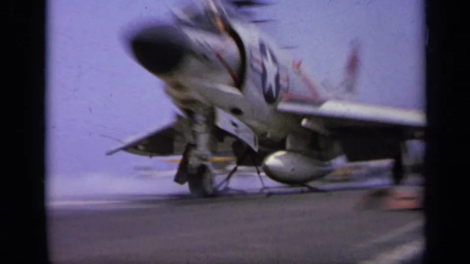 1962 Italy 8mm frame with motion blur as a military jet passes close to the camera on an aircraft carrier deck.