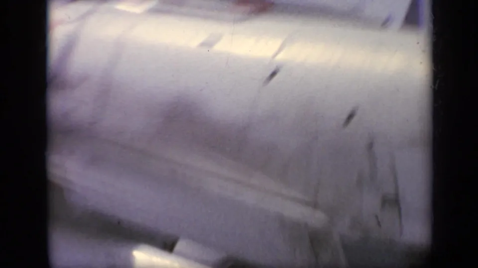 Close, soft-focus 8mm frame showing part of the white jet fuselage or wing area as it moves across the carrier sequence.