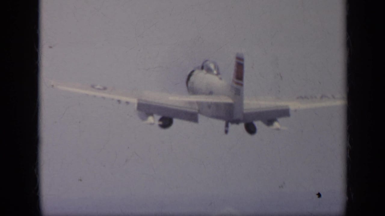 Military jet seen from behind in flight against a pale sky or sea horizon.