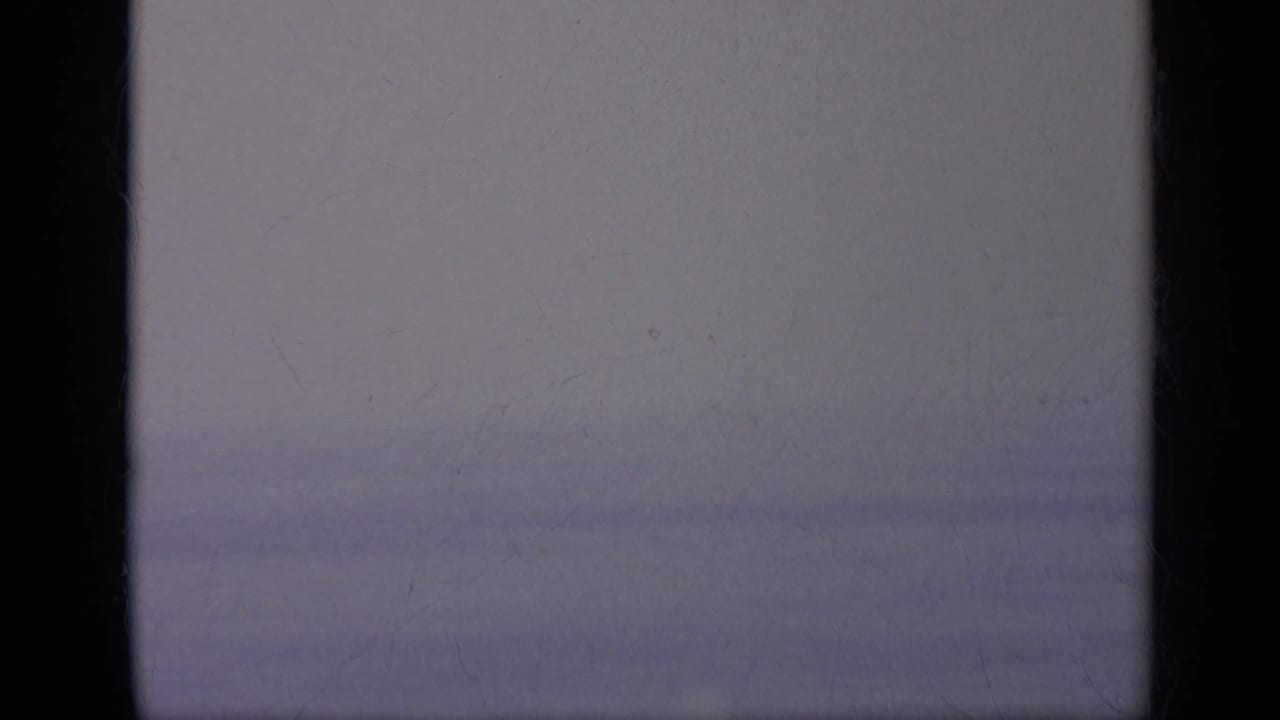 A near-blank transitional frame from the 8mm scan, with dark borders and faint sky or sea tones between aircraft shots.