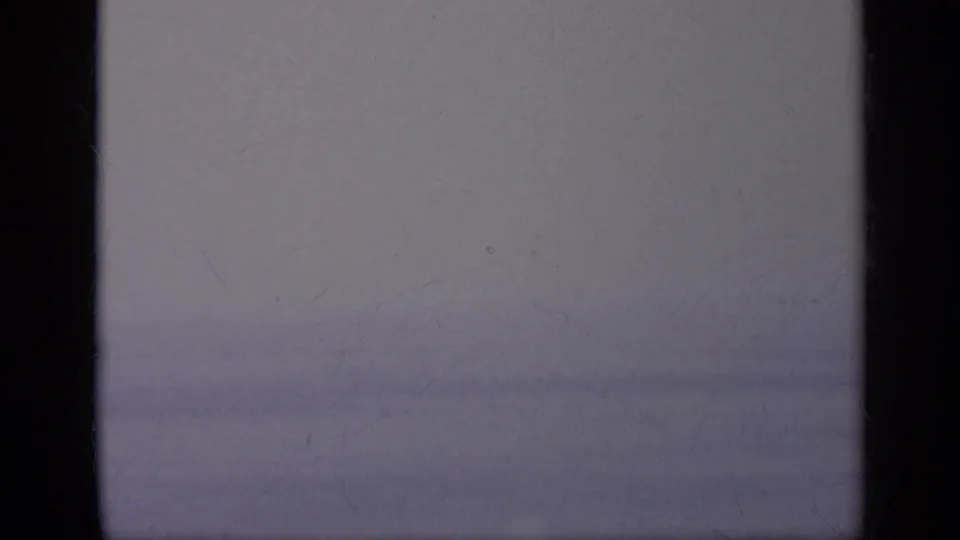 A near-blank transitional frame from the 8mm scan, with dark borders and faint sky or sea tones between aircraft shots.