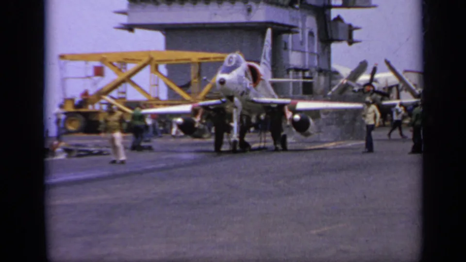 The final frame shows a white jet with red markings on a carrier deck, with crew, yellow equipment, and parked aircraft visible.