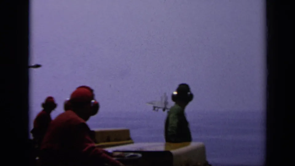 1962 Italy carrier-deck view with headset-wearing crew watching a small jet ascend over the ocean horizon.