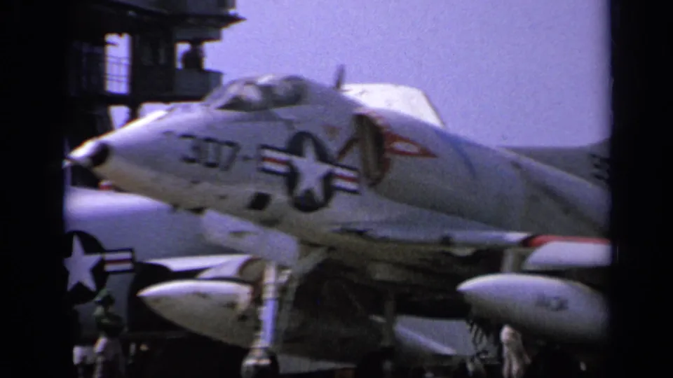 1962 Italy carrier-deck frame showing a U.S. Navy jet marked 307 with national insignia and other aircraft surfaces nearby.