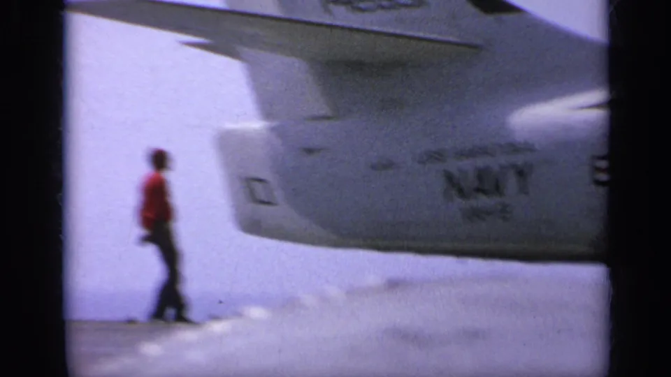 A person walks across the carrier deck near the underside of a U.S. Navy aircraft in 1962 home-movie footage near Italy.