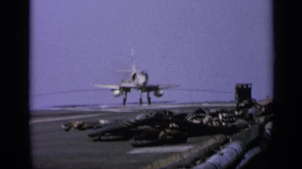 Rear view of a U.S. Navy jet on a carrier deck, with the ocean horizon and deck gear visible in faded 1962 8mm footage.