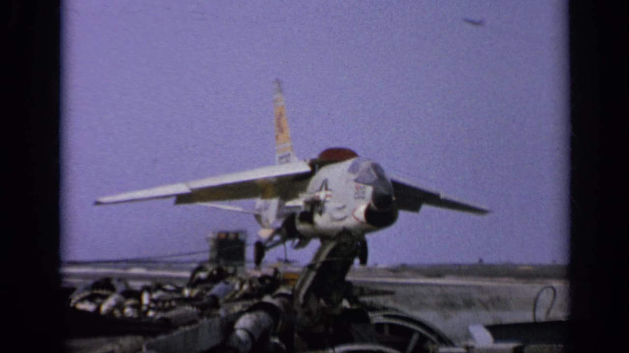 Carrier-deck view of a U.S.-marked jet, deck equipment, and distant horizon in 1962 archival 8mm footage.