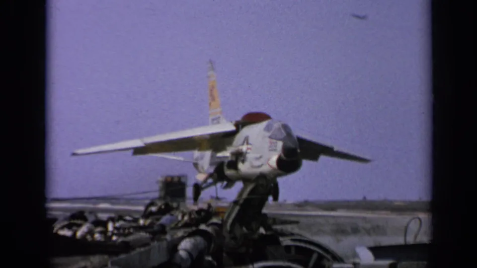Carrier-deck view of a U.S.-marked jet, deck equipment, and distant horizon in 1962 archival 8mm footage.