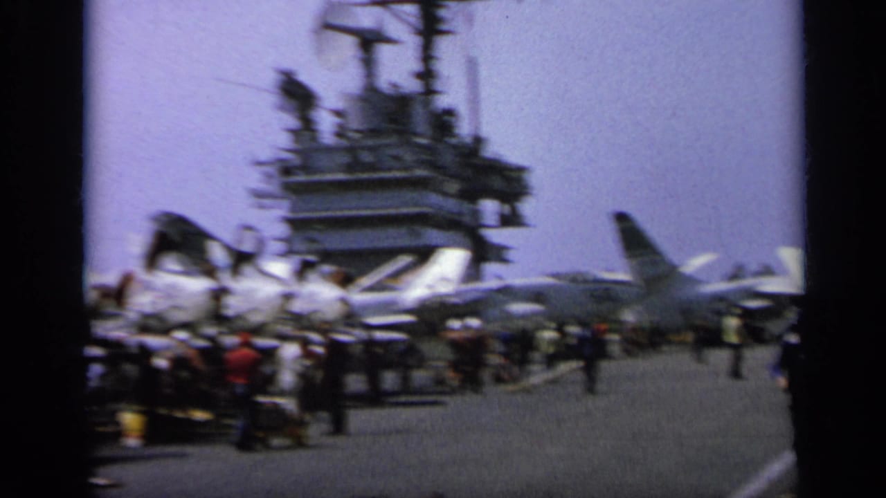 Aircraft carrier deck with jet aircraft, people, and the carrier island visible.