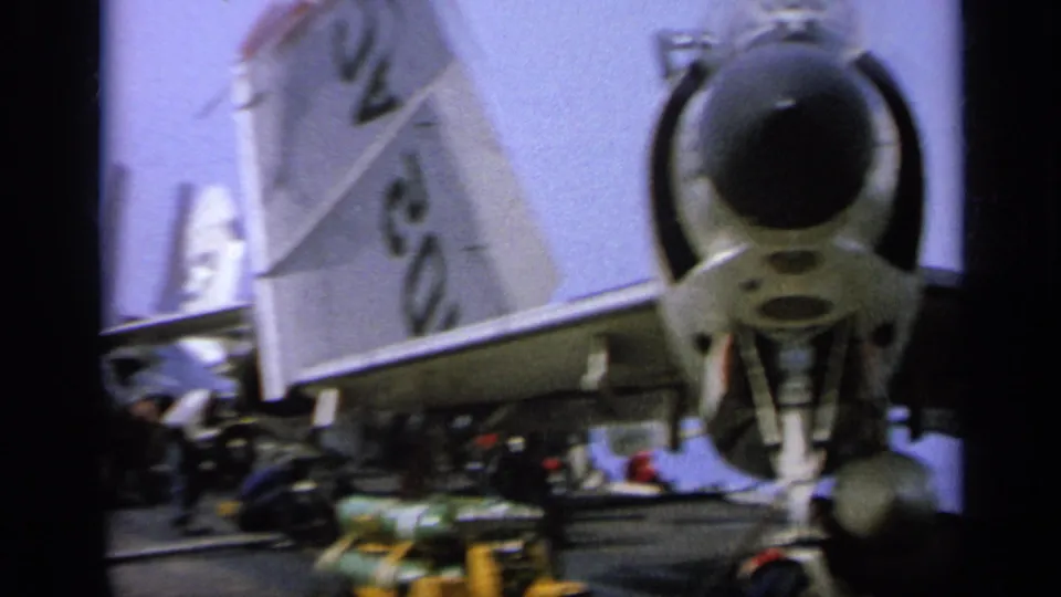 Close 8mm frame of a jet fighter's tail markings and rear fuselage area on an aircraft carrier deck in Italy.