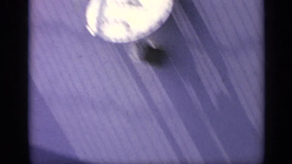 Close 1962 Italy 8mm frame with foamy water near a ridged pale boat surface, softened by motion blur and film grain.