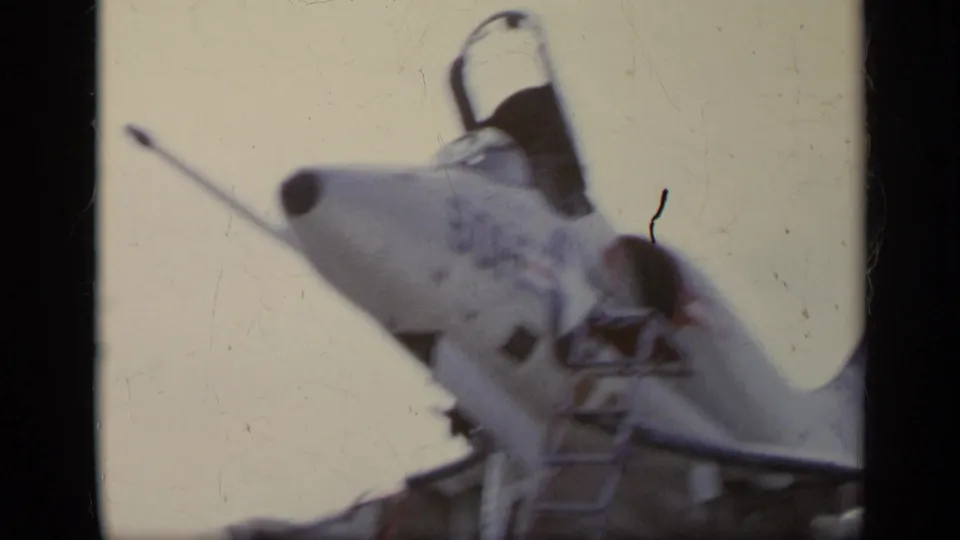 Low-angle 1962 Italy 8mm view of a fighter jet nose, open cockpit canopy, probe, and pale sky.