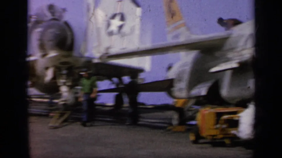 1962 Italy 8mm frame showing people near a fighter jet on a tarmac with visible markings and service equipment.
