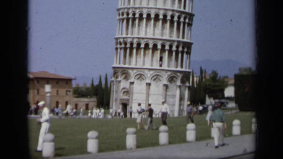 1962 8mm frame of the Leaning Tower of Pisa, tourists on the lawn and a Marine in white uniform at left.