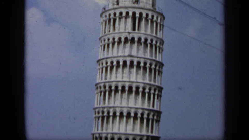 1962 Italy 8mm frame showing a cropped view of the Leaning Tower of Pisa, with arched white galleries and blue sky behind it.