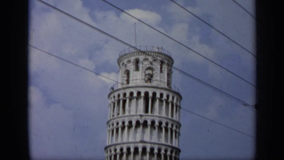 1962 Italy 8mm frame of the upper Leaning Tower of Pisa, with its bell chamber, arched galleries, blue sky, clouds, and power lines.
