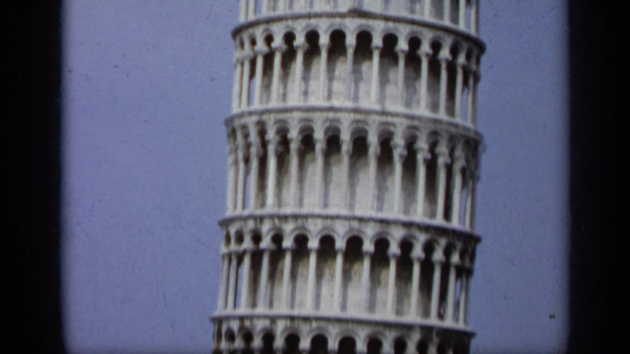 Close low-angle view of the Leaning Tower of Pisa arcades against blue sky.