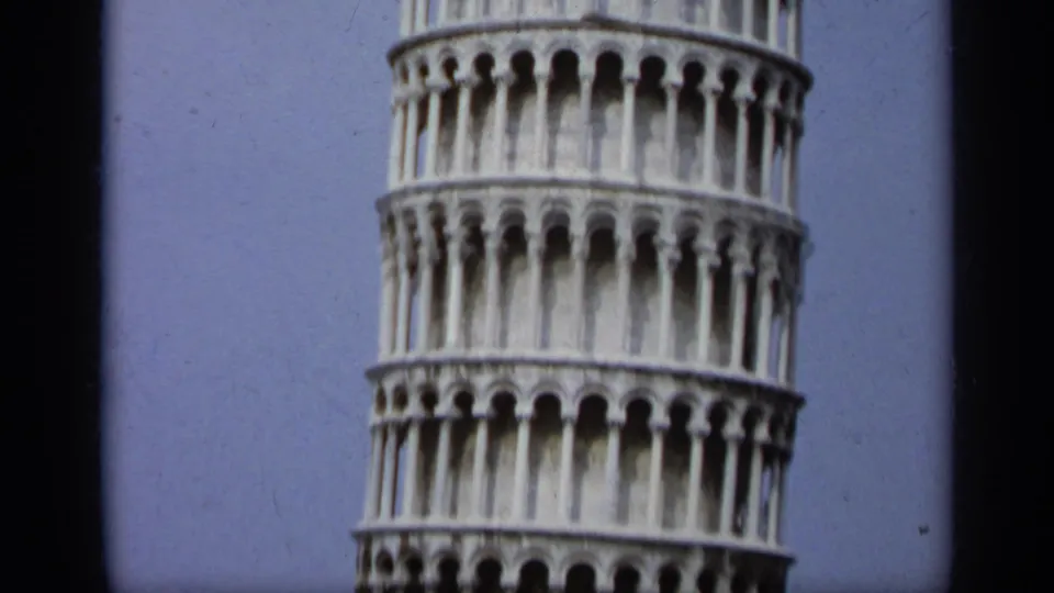 1962 Italy home-movie frame showing a close low-angle section of the Leaning Tower of Pisa with marble arcades and blue sky.