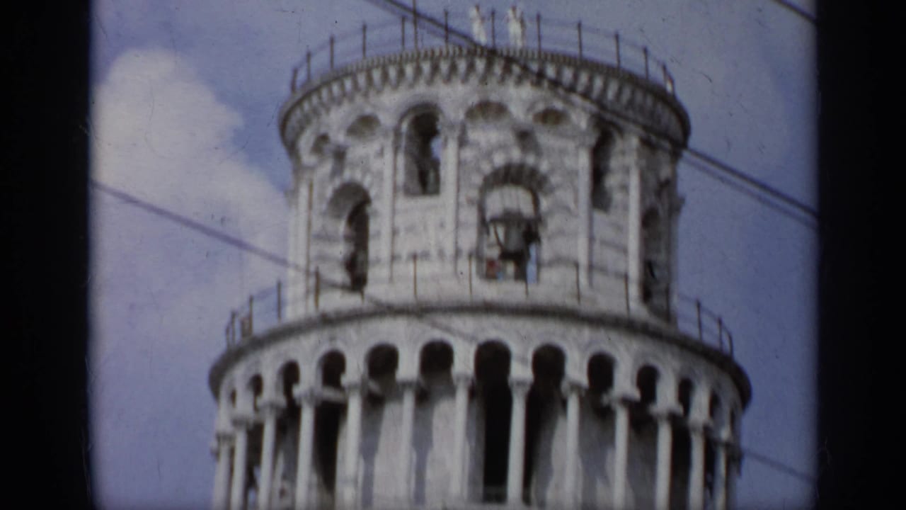 Upper section of the Leaning Tower of Pisa against a blue sky.