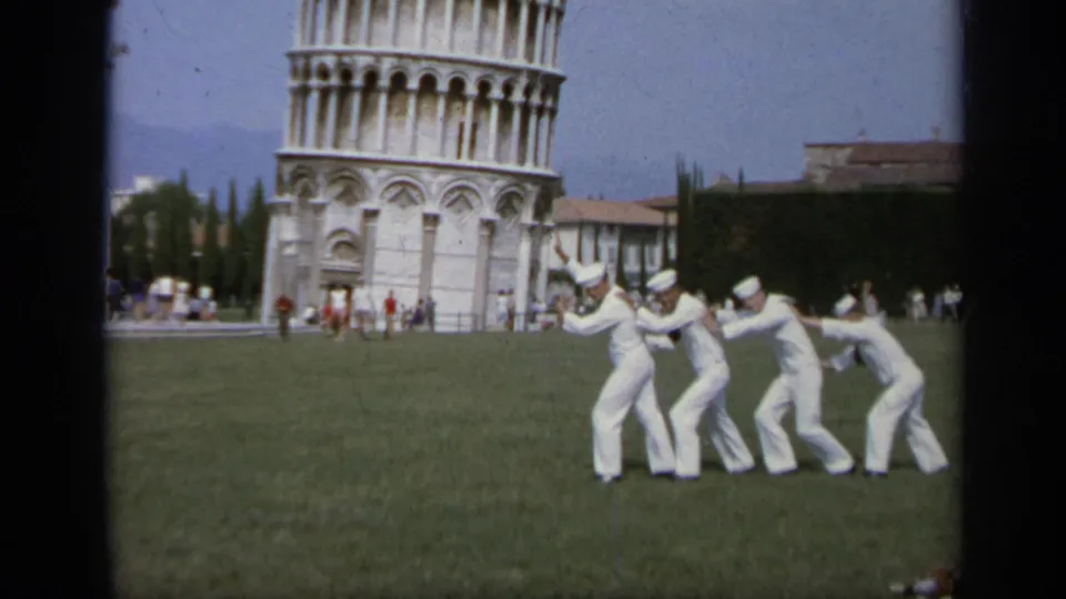 Several sailors in white uniforms form a playful leaning pose on the grass near the Leaning Tower of Pisa, 1962.