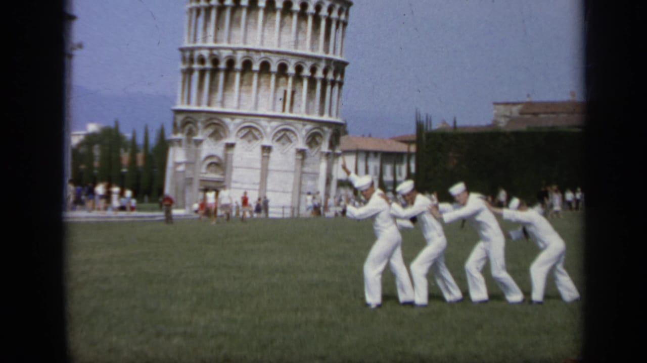 Four sailors in white uniforms lean together on a lawn before the Leaning Tower of Pisa.