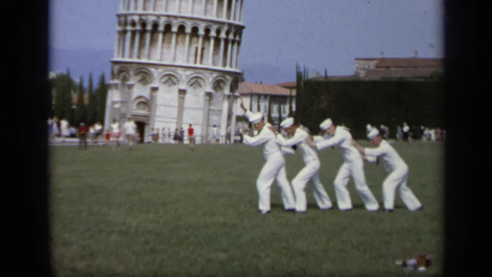 1962 Italy travel footage frame with four sailors in white uniforms playfully mimicking the tilt of the Leaning Tower of Pisa.