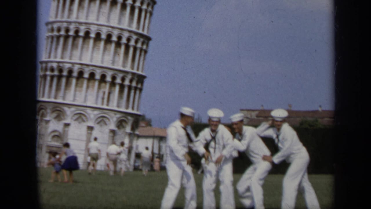 Sailors in white uniforms playfully pose on grass near the Leaning Tower of Pisa.