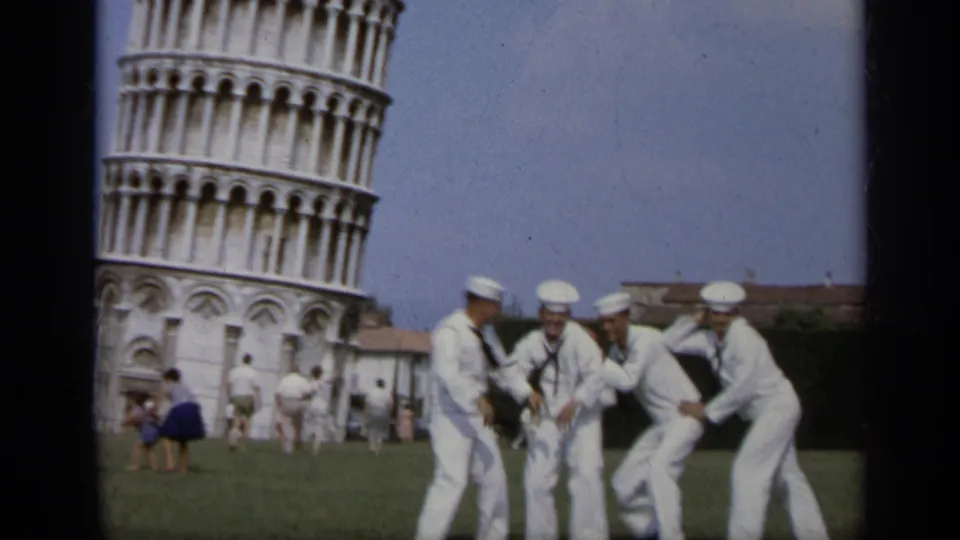 1962 Italy home-movie frame showing U.S. Navy sailors joking and posing on the lawn in front of the Leaning Tower of Pisa.
