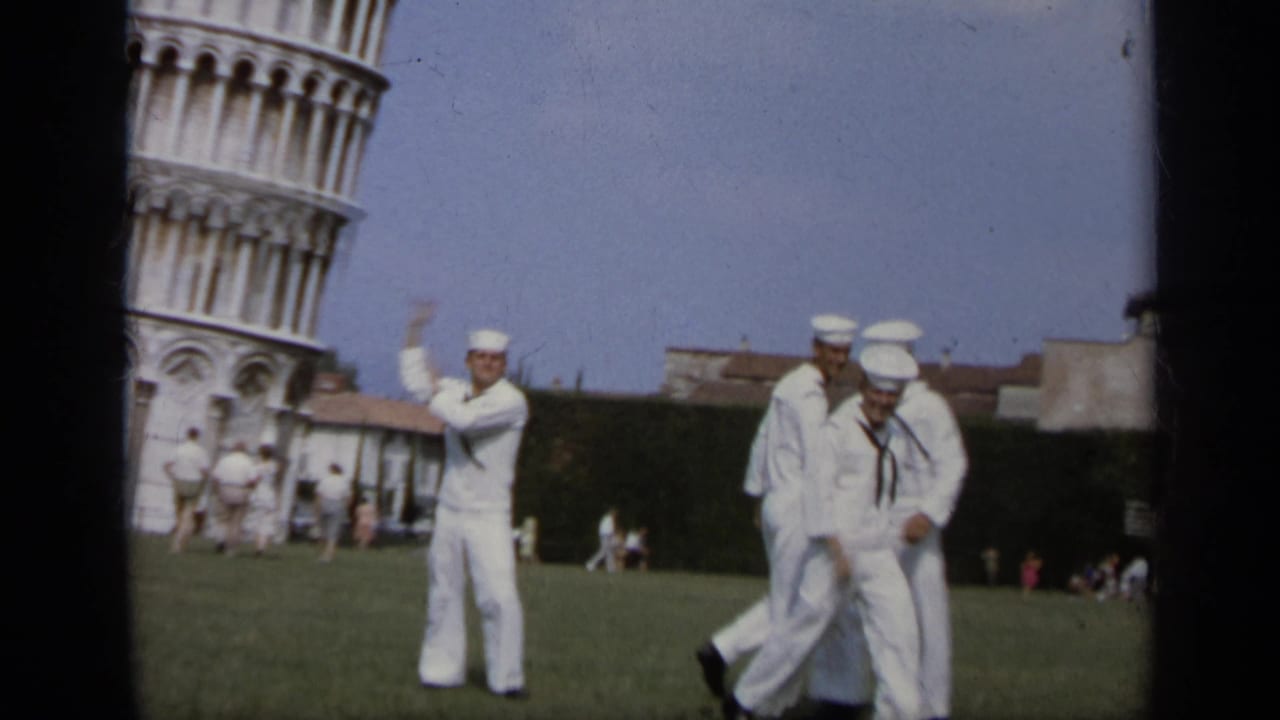A sailor gestures toward the Leaning Tower while other sailors walk nearby on the lawn.