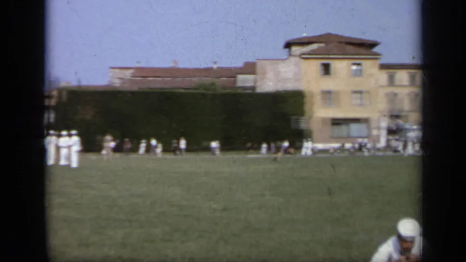 A wide 1962 Italy park view shows sailors and pedestrians spread across grass near hedges, buildings, and a distant statue.
