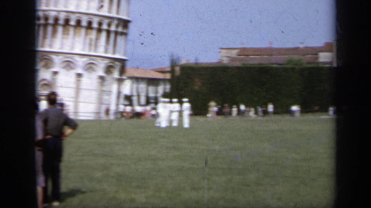 Tourists on grass near the base of the Leaning Tower of Pisa.