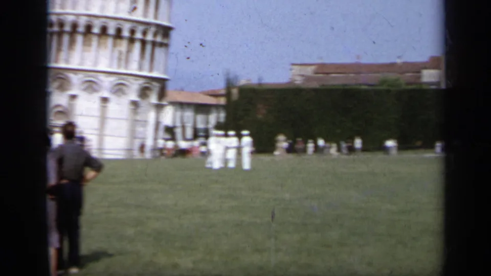 1962 8mm home-movie view of tourists and white-uniformed figures on the lawn near the Leaning Tower of Pisa in Italy.