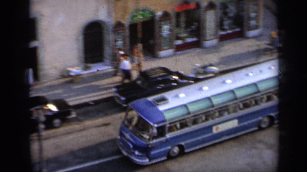 Elevated street view with a blue bus, dark cars, pedestrians, and stone buildings.
