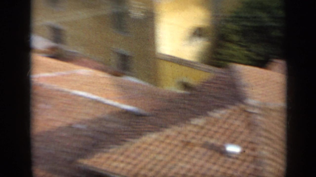 1962 Italy home-movie view looking across terracotta roof tiles toward pale city buildings from an elevated position.