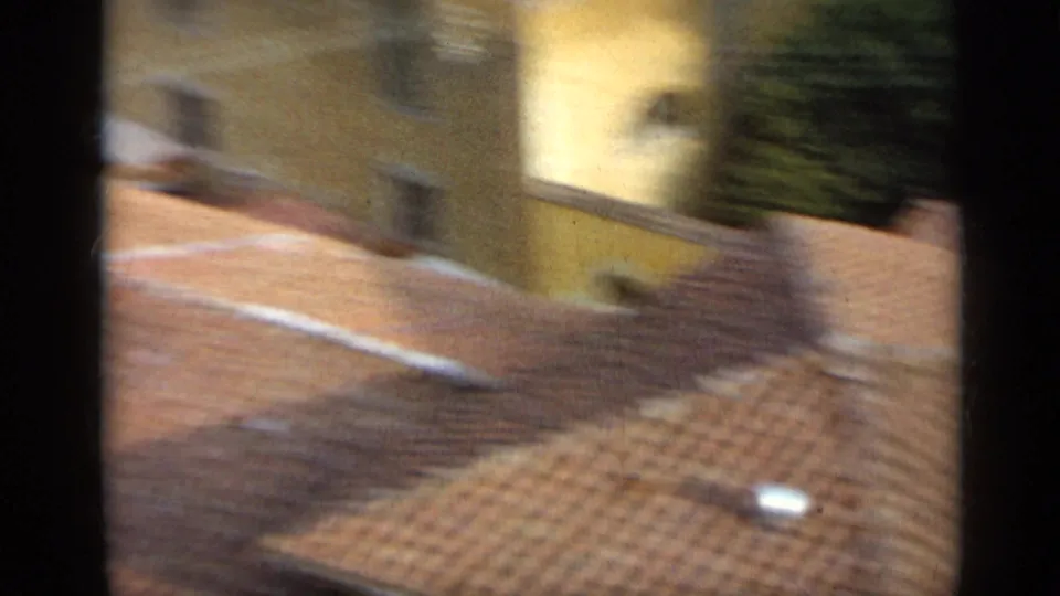 1962 Italy home-movie view looking across terracotta roof tiles toward pale city buildings from an elevated position.