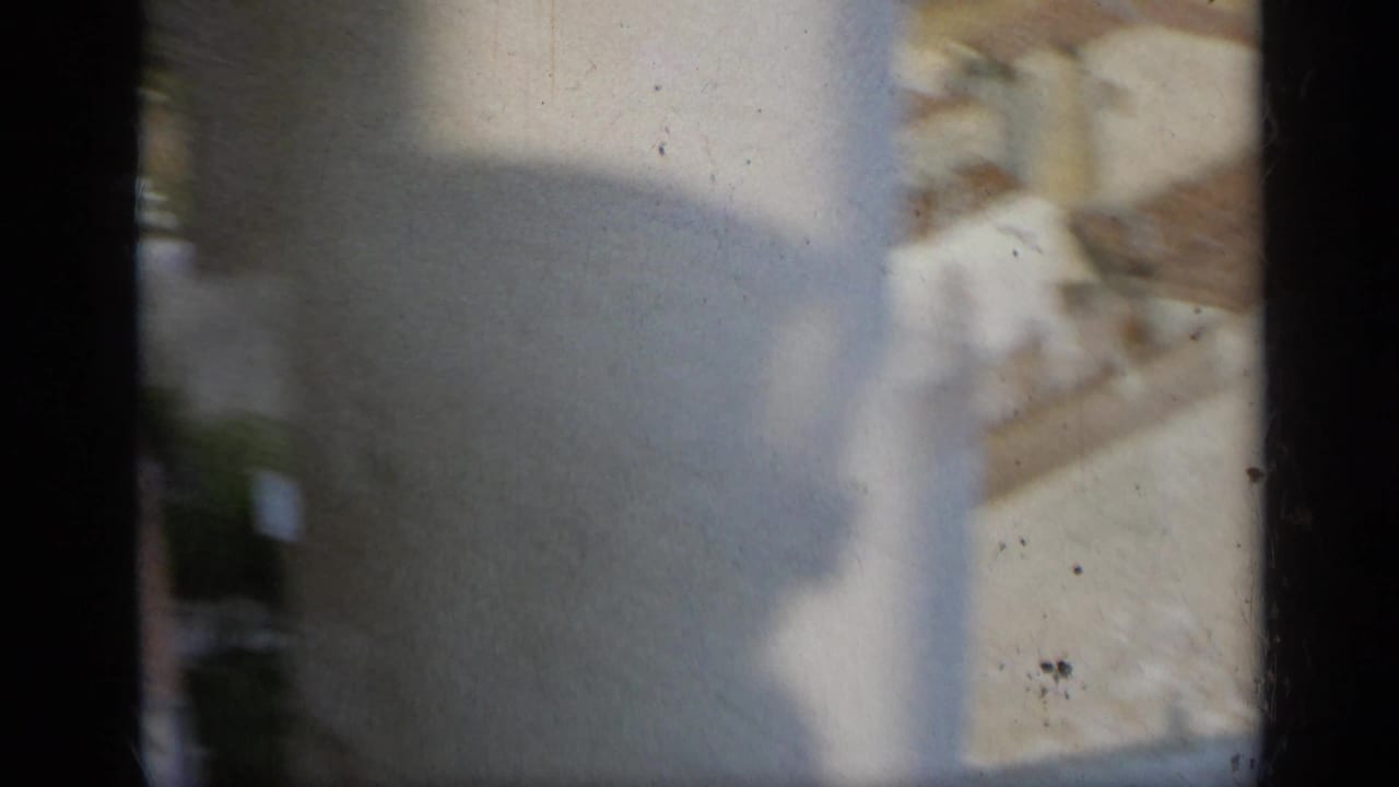 Soft, partially obscured 1962 Italy view with a pale wall, roofline, foliage, and a dark vertical column or frame edge.