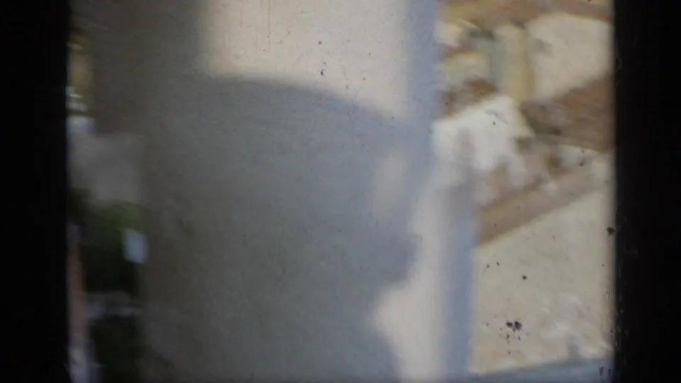 Soft, partially obscured 1962 Italy view with a pale wall, roofline, foliage, and a dark vertical column or frame edge.