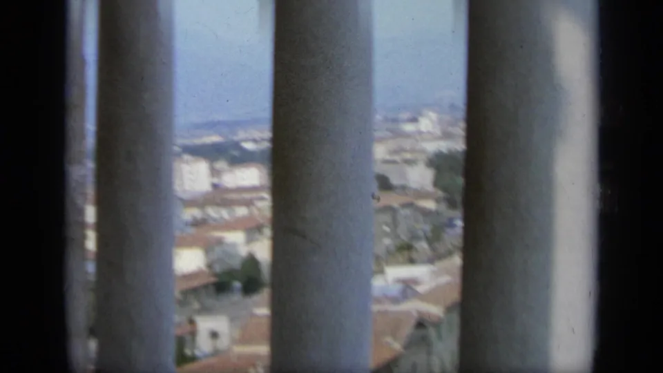 Elevated 1962 Italy city view seen through tall vertical columns, with rooftops and pale buildings blurred in the distance.