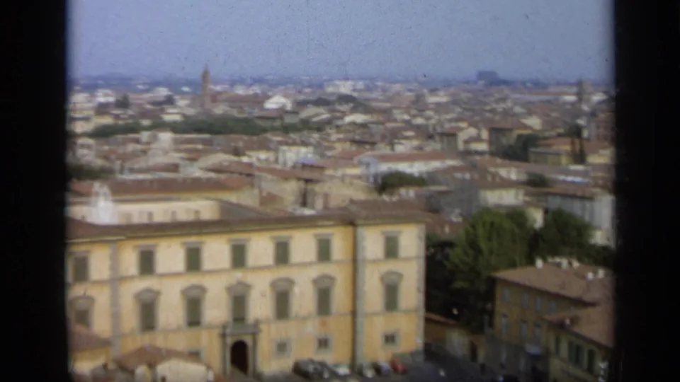Wide 1962 Italy home-movie view over a city skyline, yellow building, tiled roofs, trees, and hazy distant horizon.